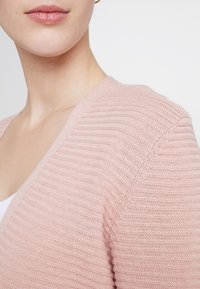 Cardigan lavorato a maglia rosa chiaro con scollatura a V e texture a costine, caratterizzato da un design sottile e dettagli delle spalle senza cuciture.