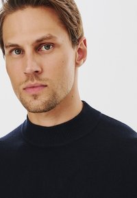 Granatowy sweter dziany z wysokim, prążkowanym kołnierzem. Materiał wydaje się miękki o gładkiej fakturze, odpowiedni do noszenia na co dzień.