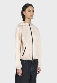Giacca leggera di un rosa chiaro con cappuccio, zip nera e tasche laterali. Il materiale ha una trama liscia con polsini elasticizzati.