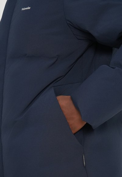 Navy puffer jacket with a smooth texture, featuring a side pocket and a small logo. The design includes a high collar and fitted sleeves.