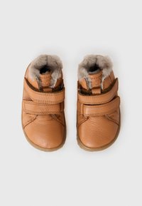 Un par de zapatos de cuero color marrón claro para toddlers, con correas de Velcro y un suave forro de pelaje, mostrados desde arriba sobre un fondo blanco.
