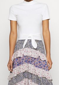 Hvid ribbet top med høj hals og korte ærmer, parret med en flerfarvet, mønstrede rynkede nederdel i blomsterdesigns og varierende farver.