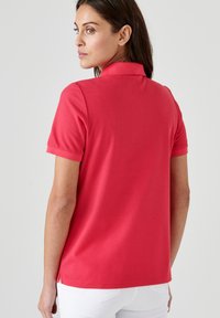Polo shirt in cotone rosso con colletto e maniche corte, caratterizzato da uno spacco laterale nell'orlo e una texture liscia.
