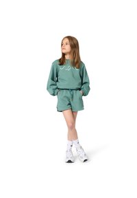 Πράσινο βαμβακερό φούτερ με μακριά μανίκια και λογότυπο, συνδυασμένο με ταιριαστό σορτς. Το μοντέλο φοράει λευκά αθλητικά παπούτσια και κάλτσες.