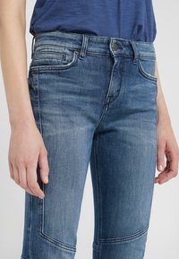 Džínové kalhoty ve středně modré barvě s vybledlým umytím. Mají pět pocket design, jemné švy a přiléhavý střih.