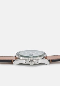 Montre en acier inoxydable avec un cadran vert, une lunette argentée et un bracelet en cuir brun. Comprend un boîtier rond, une couronne et des index horaires.