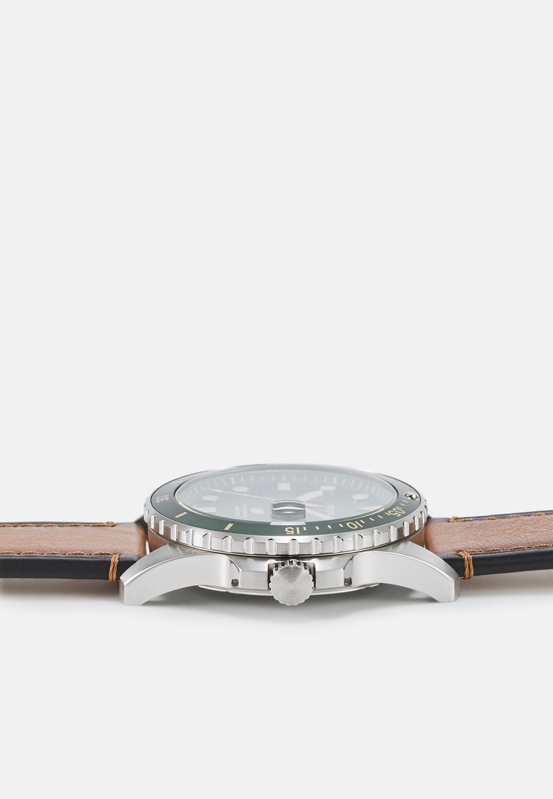 Edelstahl-Uhr mit grünem Zifferblatt, silberner Lünette und braunem Lederarmband. Verfügt über ein rundes Gehäuse, eine Krone und Stundenmarkierungen.