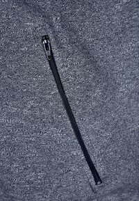 Šedá fleece mikina se zipem, vyrobená z texturované tkaniny. Zipper je černý a umístěný šikmo. Povrch vykazuje jemný melírovaný vzor.