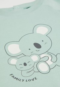 Miętowa bluza z nadrukiem przedstawiającym dwóch koali. Tekstura jest żebrowa z białymi akcentami, a poniżej znajduje się napis "MIŁOŚĆ RODZINNA".