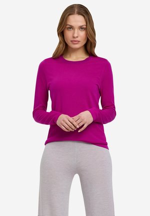 Langärmliges fuchsia Hemd aus weichem Material, mit Rundhalsausschnitt und lockerer Passform. Getragen mit hellgrauen Hosen.