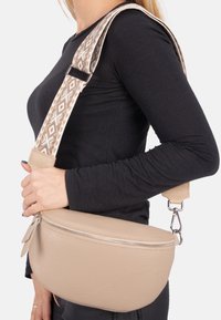 Beige Leder Crossbody-Tasche mit einer strukturierten Oberfläche; verfügt über einen gemusterten, verstellbaren Riemen und einen silbernen Reißverschluss mit einer Stoff-Zuglasche.
