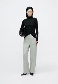 Sort langærmet top med forlænget skørt, kombineret med grå højtaljede viddebukser og en sort clutch taske. Sorte spidse hæle.