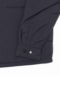 Manche de veste matelassée foncée avec deux boutons-pression au poignet et détails de couture visibles.