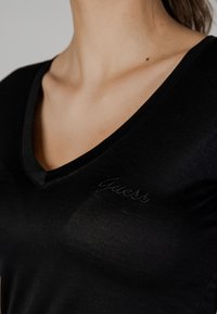 Sort v-hals t-shirt lavet af blødt, strækbart stof med en tætsiddende design. Har diskret "Guess" broderi ved halsen.