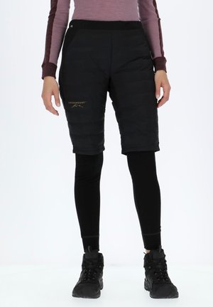 Black insulated shorts with a puffy design, paired with black leggings. Notable gold branding on the left thigh. Rugged black hiking boots.