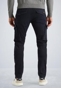 Donkerblauwe cargobroek met zijzakken, taps toelopende pijpen en contrasterende stiksels. Gepaarde met witte sneakers met een tan kleurige hakaccent.