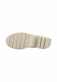 Semelle de chaussure beige clair avec caoutchouc texturé, présentant des rainures horizontales et un petit logo. Forme plate, design minimal et matériau durable.