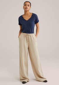 Tumši zils V-veida kakla T-krekls ar sarullētām piedurknēm, apvienots ar bēšiem plašiem biksēm, ar elastīgu jostasvīru un auklu.