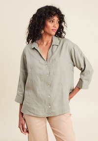 Lichtgroen linnen shirt met een kraag, knoopsluiting en een enkele borstzak. Heeft mouwen tot de elleboog en een ontspannen pasvorm.