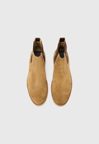 Botines de ante marrón con recortes laterales y acentos de cuero, que presentan una textura suave y un diseño de punta redonda.