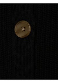 Czarny sweter robiony na drutach z dużym, okrągłym, jasnym guzikiem z czterema otworami, podkreślający teksturowany materiał.