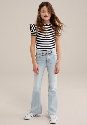 Top de manga corta a rayas en blanco y negro con hombros rizados, combinado con unos vaqueros de campana de color azul claro y zapatillas blancas.