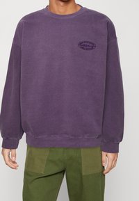 Lila sweatshirt i bomull med rund halsringning, ribbade ärmslut och en liten tryckt logotyp på bröstet. Standardpassform och mjuk textur.