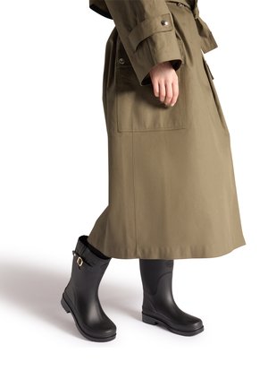 Zwarte rubberen regenlaarzen met een gespdetail, gedragen bij een olijfgroene lange jas. De laarzen hebben een gestructureerde zool en een gladde afwerking.