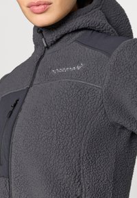 Siva polar bunda z zgoščenim površjem, z zadrgo spredaj in kapuco. Ima črne podrobnosti in logo na področju prsi.