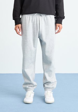 Person wearing light gray sweatpants with elastic cuffs, white sneakers, and a black long-sleeve top, standing on a blue floor.