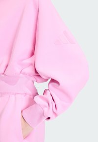 Ružová mikina s elastickým pásom a manžetami, textúrovaná tkanina a nenápadný detail loga na rukáve. Nastaviteľný strih.