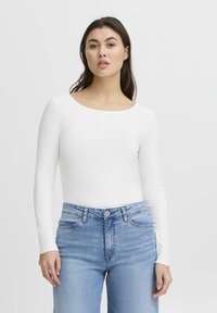 White long-sleeve top with ribbed texture and a wide neckline, paired with light blue high-waisted jeans featuring front pockets and a button closure.