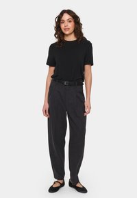 Sort T-shirt med korte ærmer, kombineret med høj talje mørkegrå bukser og sorte flade sko. Outfitet har et enkelt, afslappet design.