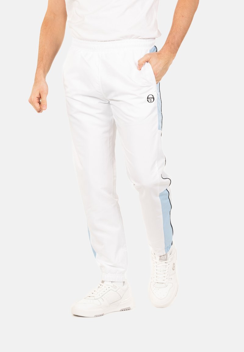 Pantalons de sport blancs avec des rayures latérales bleues et noires, taille élastique et poches latérales, associés à des baskets blanches.