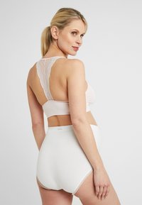 Lichtroze bralette met kant aan de achterkant en witte hooggetailleerde onderbroek met kantafwerking. Glad materiaal met een aansluitend ontwerp.