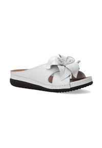 Hvide lædersandal med slip-on design, der har udskårne sider og en stor sløjfe. Den har en brun indersål og en sort tekstureret gummisål.