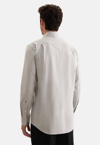 Camicia da uomo grigia chiara con bottoni, caratterizzata da maniche lunghe, colletto standard, texture liscia e piccolo logo dettagliato su ciascun polsino.