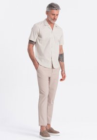 Beige Kurzarmhemd mit Kragen, kombiniert mit hellbeigen Slim-Fit-Hosen und grauen Slippern. Subtile Textur und klares Design.