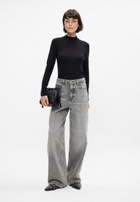 Melnas pieguļošas turtlenecka formas blūze, augsto jostasvietu gaiši pelēkas platas kājas džinsi, melna krokotā rokassoma un norādītas melnas kurpes ar sudraba rotājumiem.