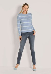  Lichtblauw gestreepte gebreide trui met ribbelstructuur, gecombineerd met donkere skinny jeans en blauwe hakken, met een rafelige zoomafwerking. 