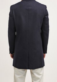 Marinblå ullöverrock med skräddarsydd passform, enkel klyfta bak och tvåknappshållare. Slät textur, elegant silhuett och klassisk design.