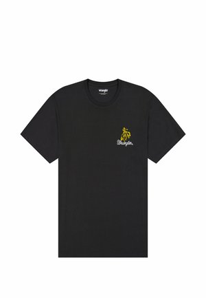 Camiseta de algodón negra con un gráfico amarillo de un jinete a caballo y el texto "Wrangler" debajo, mangas cortas y diseño de cuello redondo.