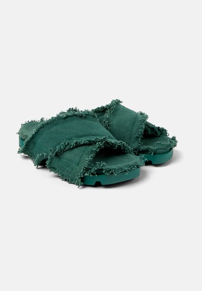 Gröna tygslip-in sandaler med fransiga kanter, korsande remmar och gummisulor, med en texturerad yta och en avslappnad design.