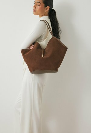 Borsa tote in suede marrone con una texture morbida, dotata di un'ampia apertura superiore e di una maniglia sottile, arricchita da un accento in tonalità oro.