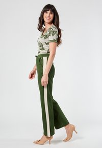 Knit top with green butterfly print, paired with olive green pants featuring a cream stripe. Model wears nude heels, showcasing a casual look.
