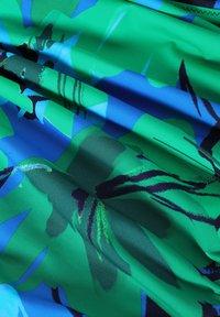 Multicolore stof met grote groene en blauwe bloemmotieven, met donkere omlijningen en een gladde, licht reflecterende textuur.