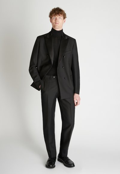 Zwart dubbelgebreid colbert met satijnen kraag, gecombineerd met een zwarte coltrui en bijpassende broek. Soepele stof, moderne getailleerde pasvorm.