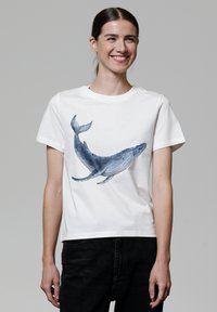 Weißes Baumwoll-T-Shirt mit einem blauen Wal-Design auf der Vorderseite. Das Shirt hat einen Rundhalsausschnitt und kurze Ärmel, mit einer lockeren Passform.