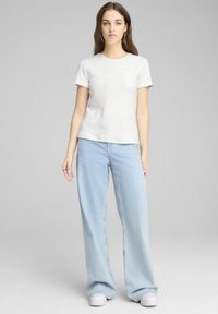 Camiseta blanca de manga corta con un acabado texturizado, combinada con jeans de pierna ancha azul claro y zapatillas blancas. Diseño simple y ajuste casual.