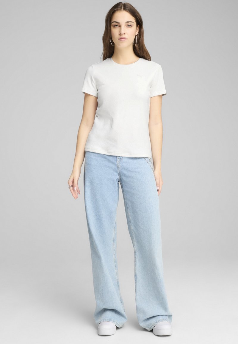 Camiseta blanca de manga corta con un acabado texturizado, combinada con jeans de pierna ancha azul claro y zapatillas blancas. Diseño simple y ajuste casual.